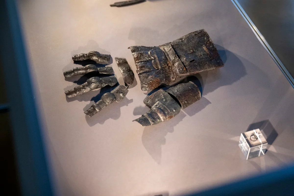 Bruchstücke eines Panzerhandschuhs liegen in einer Vitrine.